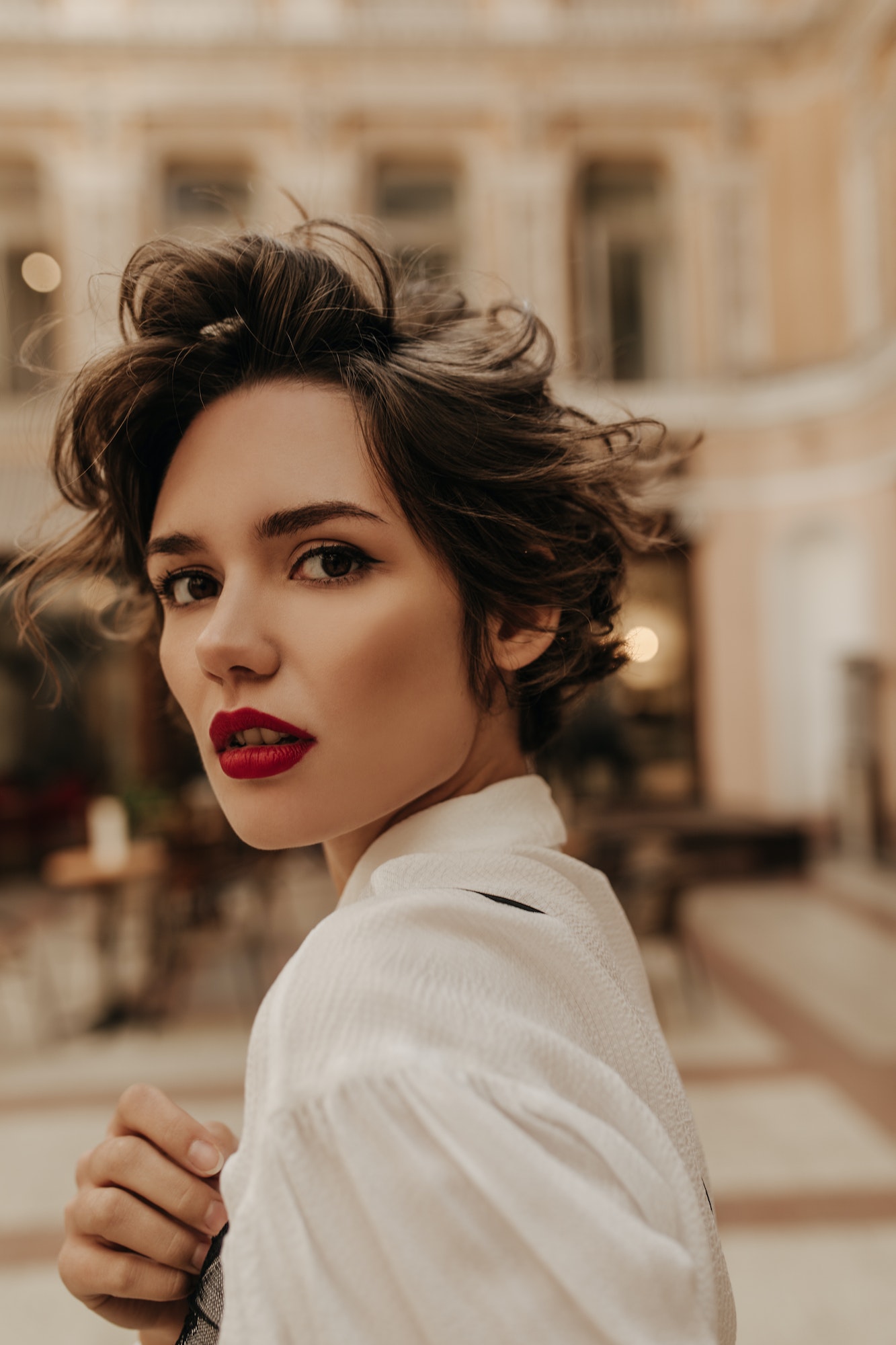 Beautiful lady with wavy short hairstyle looking into camera at street. Cool woman with red lips in